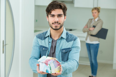 young man holding model house made from euro banknotesの写真素材