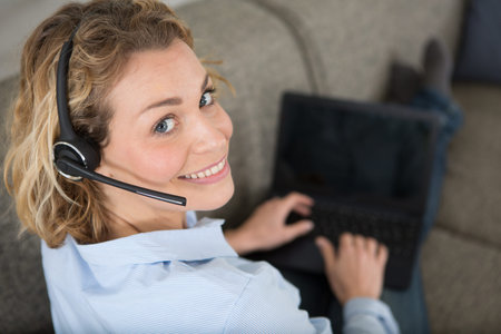 freelance worker on sofa using laptop and wearing headset