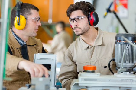 workers with earmuffs and goggles operating machine