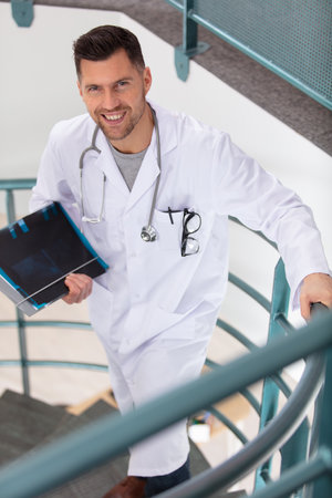 smiling doctor carries folder as he walks up stairsの写真素材