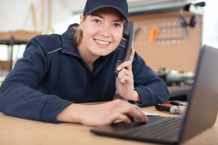 woman in workshop using laptop and talking on landline