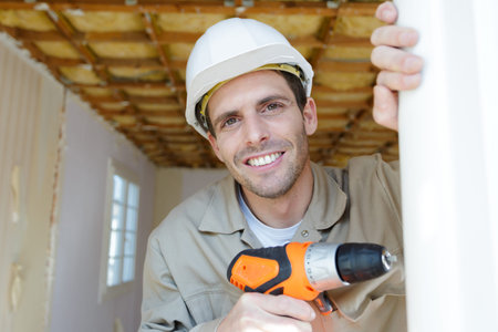 handsome young man holding electric drill and smiling at cameraの写真素材