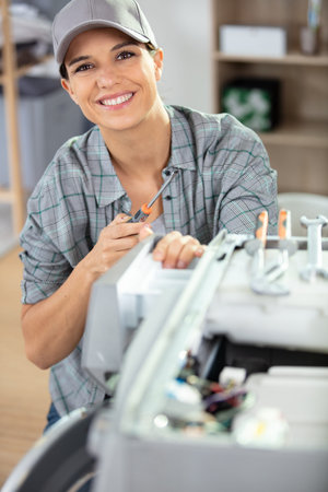 woman is using a screwdriver to fix washing machine