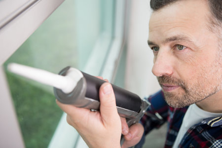 happy man using a silicone gun to repair a windowの写真素材