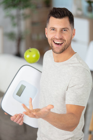 cheerful man holding bathroom scales throws apple into the airの写真素材