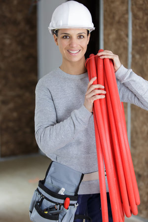female builder carrying reel of red pipe on her shoulder