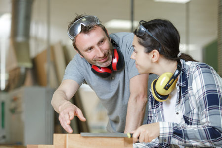 man explaining woman woodworking tips in wood workshop