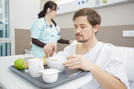 male patient eating meal in hospital bedの写真素材