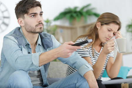 upset woman looking at tired man on sofa watching tvの写真素材