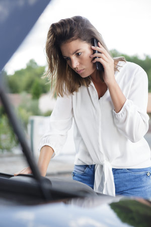 broken down woman looking under hood and using smartphone