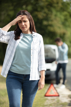 upset woman near warning triangle and broken car