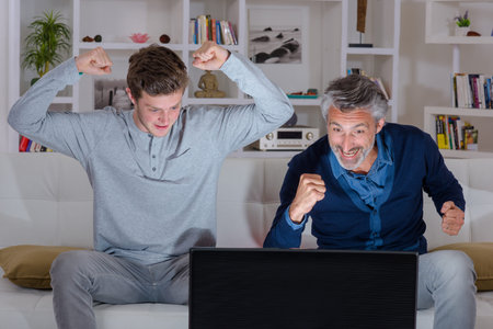 Father and son watching television, making victory gestures