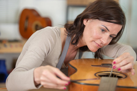 young woman as luthier holds guitar spare part for repairの写真素材