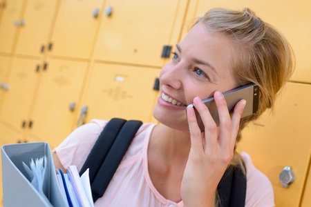 female student using mobile phone in locker roomの写真素材