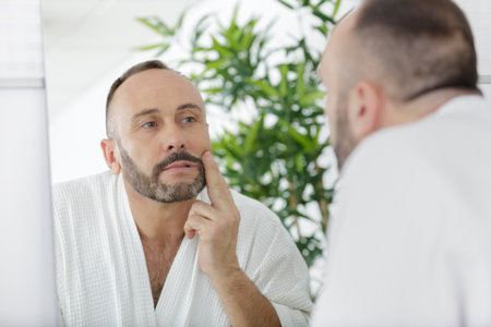 man touching beard and face looking in mirrorの写真素材