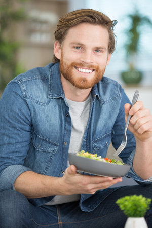 happy young man eating a saladの写真素材