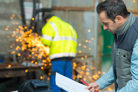 man looking at paperwork colleague using angle grinder in background