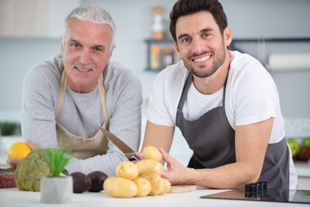 adult son and senior father cooking indoors at homeの写真素材