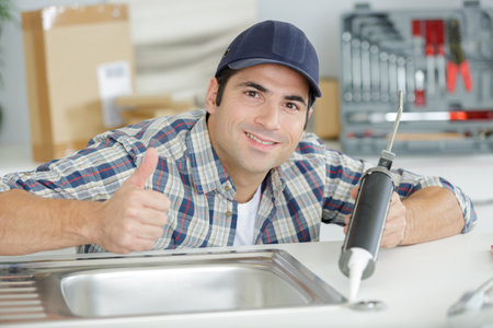 handyman is working with caulking gun under the sinkの写真素材
