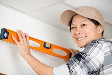 happy young female worker holding level on a ceilingの写真素材