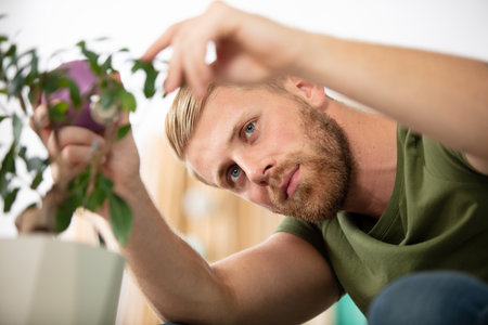attractive young man in apartment watering plantの写真素材