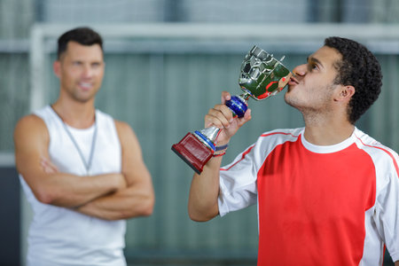 young sportsman kissing trophy coach in backgroundの写真素材