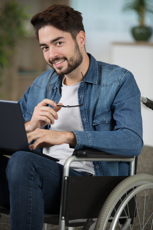 disabled young man sitting in wheelchair using laptopの写真素材