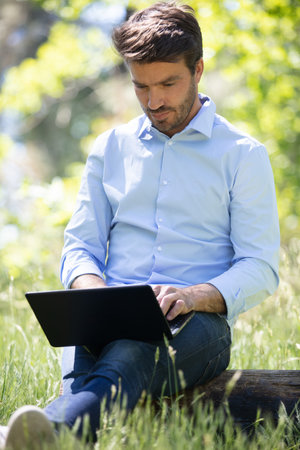 businessman sitting on the grass is working on laptop