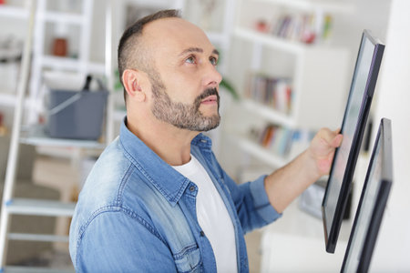 man hanging picture frames in his homeの写真素材
