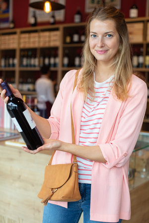 young woman is choosing a wine bottleの写真素材