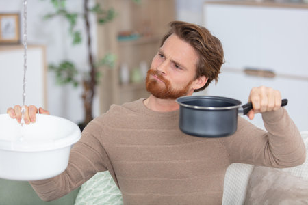 man holding plastic basin under water leakage from ceilingの写真素材