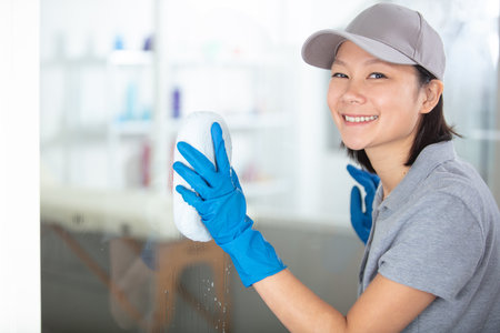 portrait of happy young maid cleaning glass with spongeの写真素材
