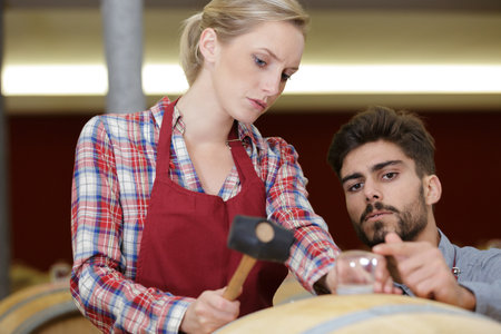 young woman using a hammer with male winemakerの写真素材