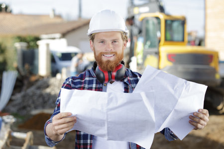 carpenter consulting blueprints in front of construction siteの写真素材