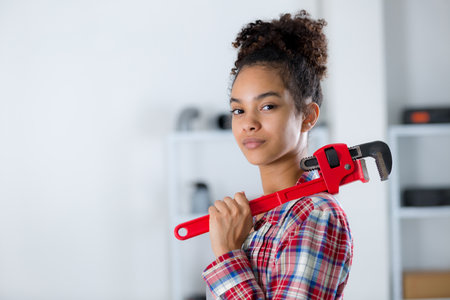 confident young woman carrying adjustable wrench over her shoulderの写真素材