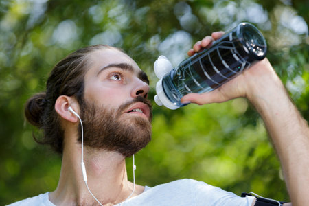 tired man drinking a bottle of water in the forest