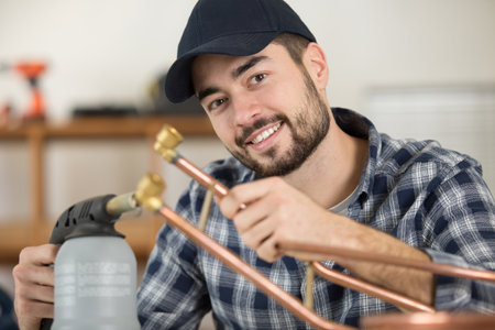 smiling plumber using welding gas torch to solder copper pipesの写真素材