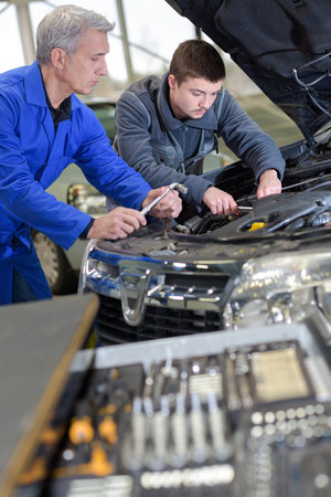 teacher helping student training to be a car mechanic