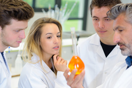 Students looking at colored liquid held by teacherの写真素材