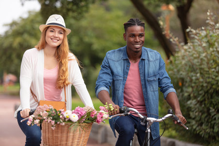 happy young couple riding bicycles with flowers in basketの写真素材