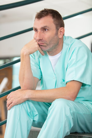 depressed male nurse sits alone on staircaseの写真素材