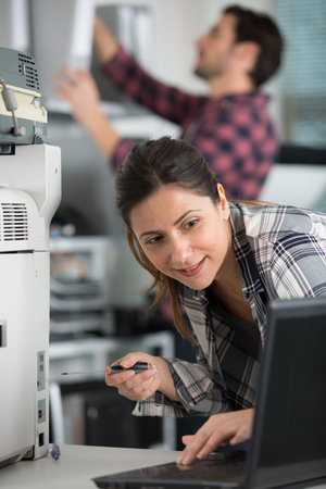 technician using a laptop while repairing a photocopier