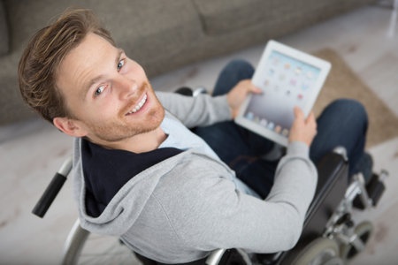 happy young man in a wheelchair holding a tablet pc