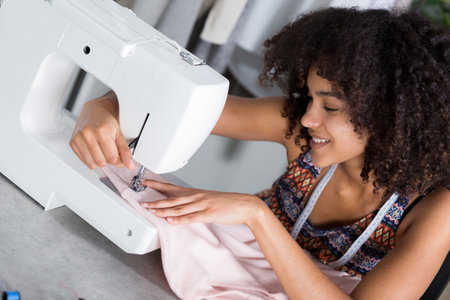 happy girl seamstress sitting and sews on sewing machineの写真素材