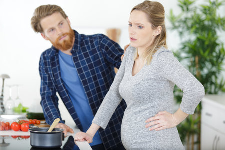 husband taking care of pregnant wife with-back-ache in the kitchenの写真素材