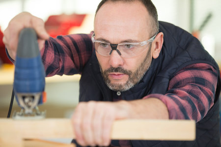 man using electric jigsaw to cut pine timberの写真素材