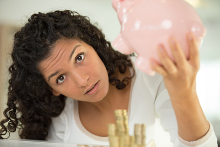woman looking questioningly at her piggy bankの写真素材