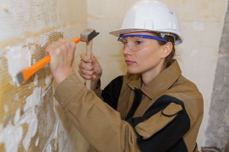 female builder using hammer and chisel on wallの写真素材