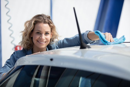 young woman dry wiping her car with microfiberの写真素材