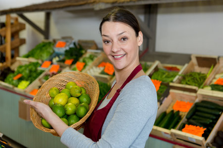 female greengrocer holding basket of limesの写真素材